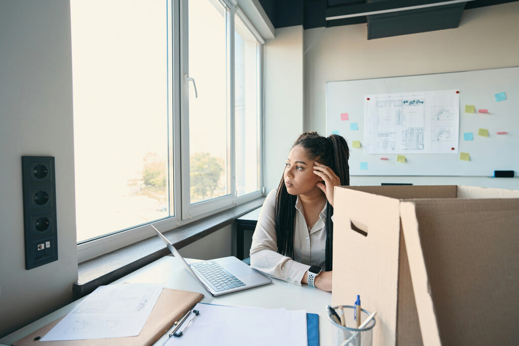 Uma mulher contemplativa em frente a janela do trabalho e decidindo se sai da empresa
