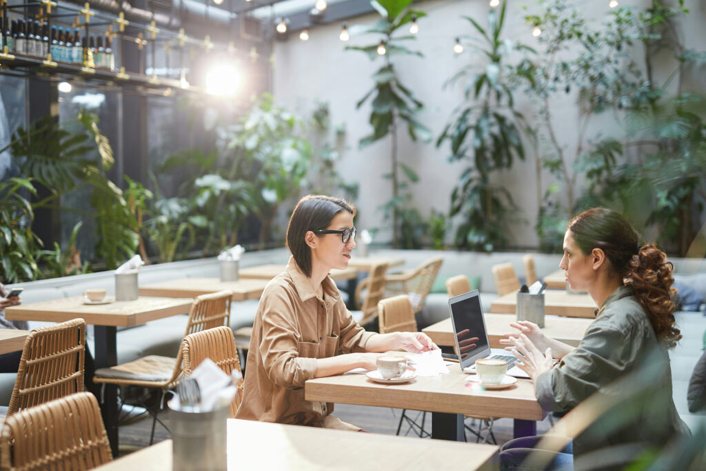 duas mulheres trabalhando na mesa de um cafe, representando o trabalho híbrido